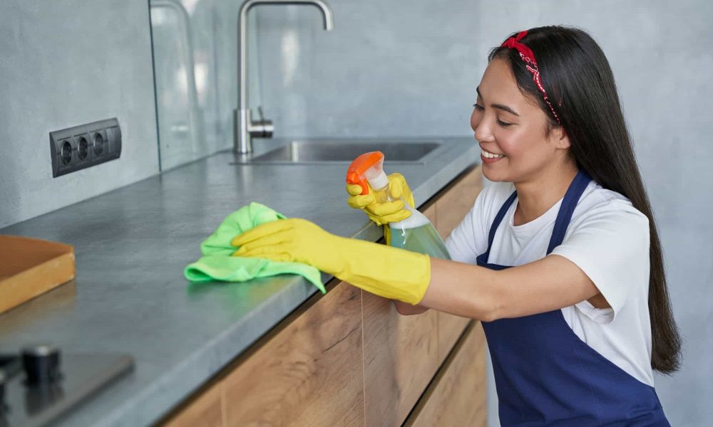 Happy young woman, cleaning lady smiling while cleaning the kitchen