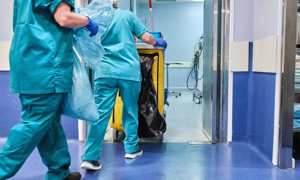hospital cleaning staff enter an operating room with a cleaning cart.